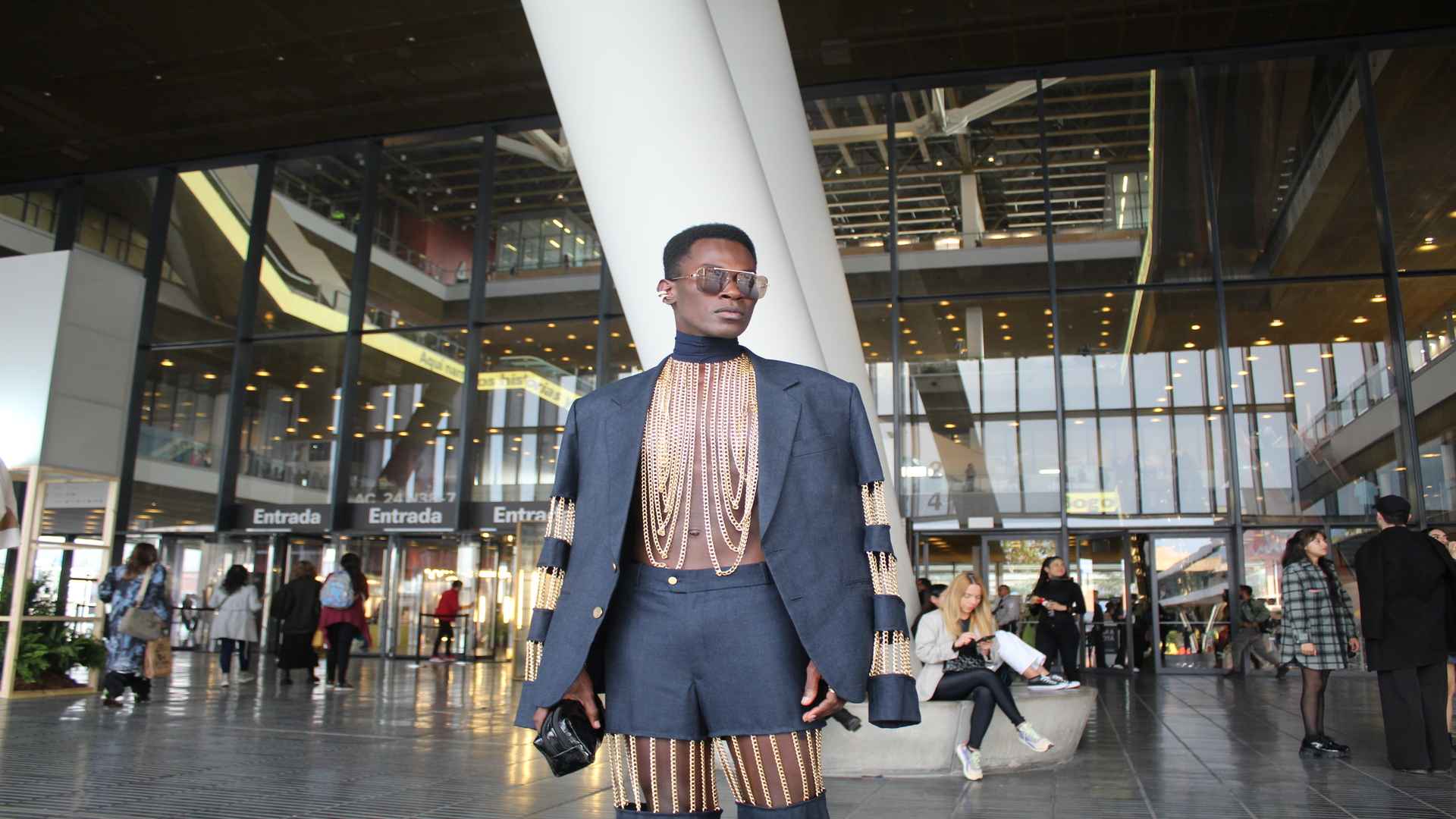 Persona con estilo único BFW. Traje azul con detalles dorados, gafas de sol. Moda de vanguardia en Bogotá.